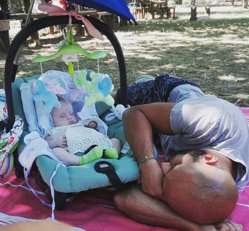Luca Trapanese laying in a park while his daughter is asleep in a car seat