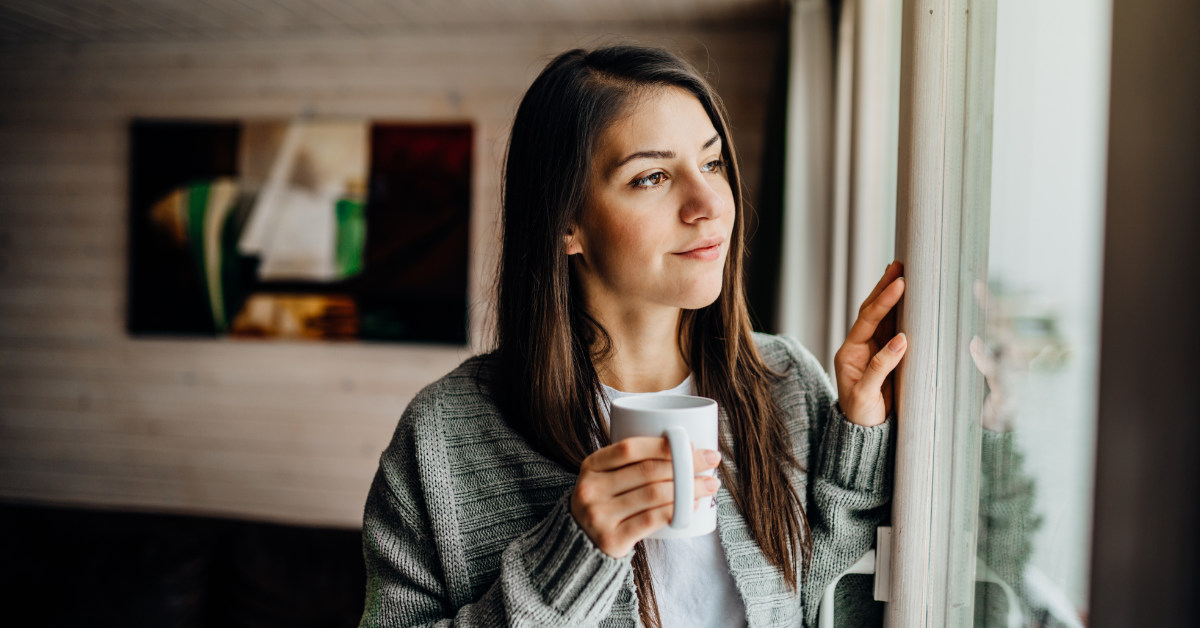 woman looking out the window holding a cup of coffee