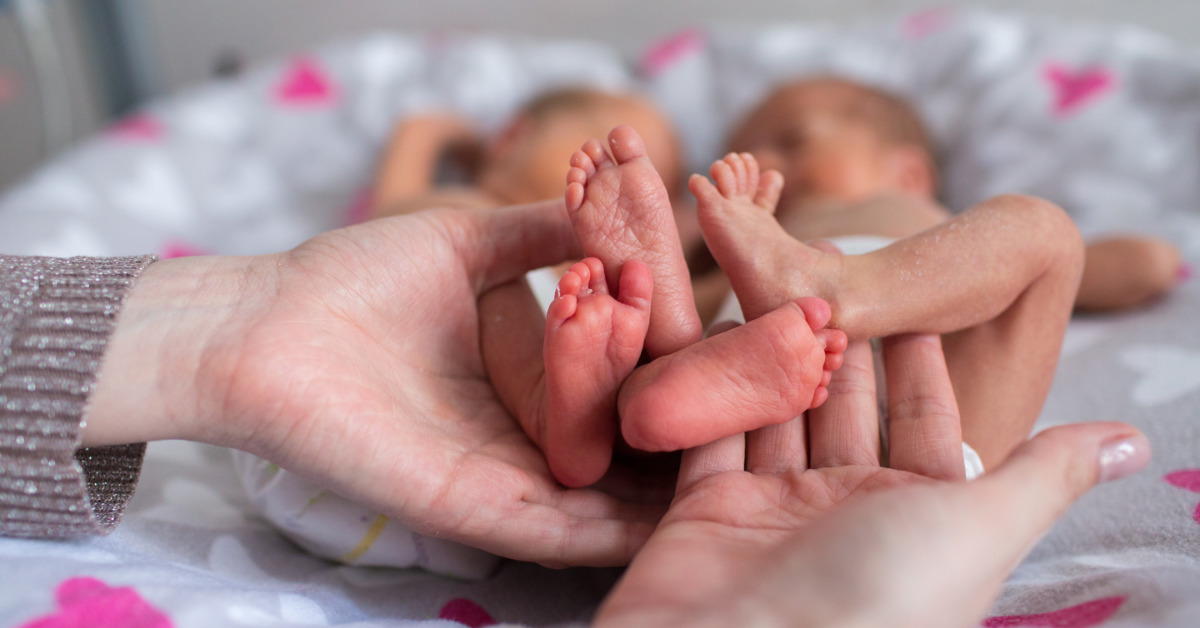 hands holding two pairs of very small infant feet