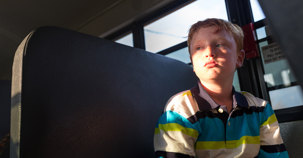 young boy sitting alone on a school bus seat