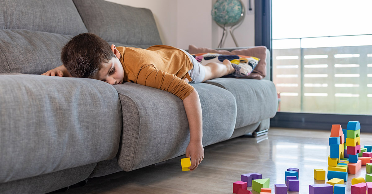 child laying on couch on stomach. HIs extends down over the side holding a yellow toy block