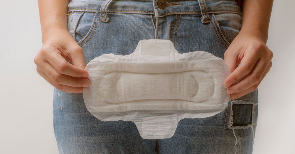 person wearing jeans holding large menstrual pad in front of groin area 