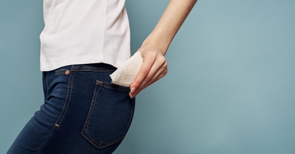 person putting menstrual pad in back pocket 
