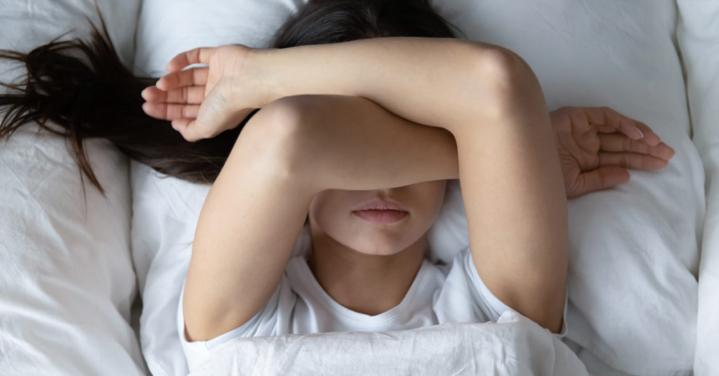 woman laying in bed with arms cross over head 