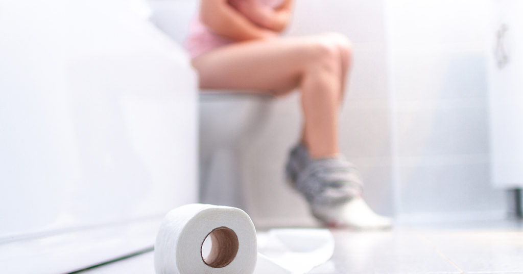 toilet paper on floor with person on toilet in background out of focus 