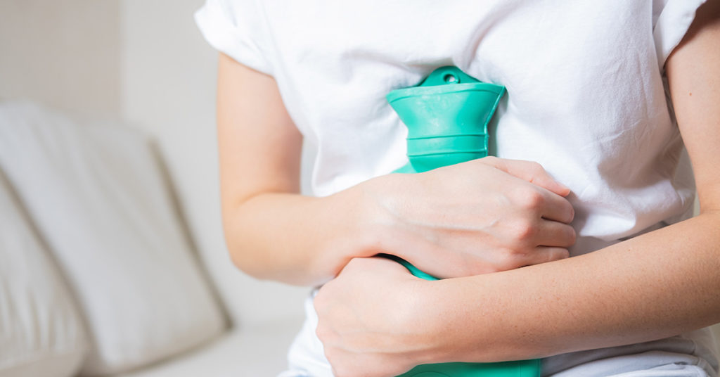 person placing hot water bottle over abdomen 