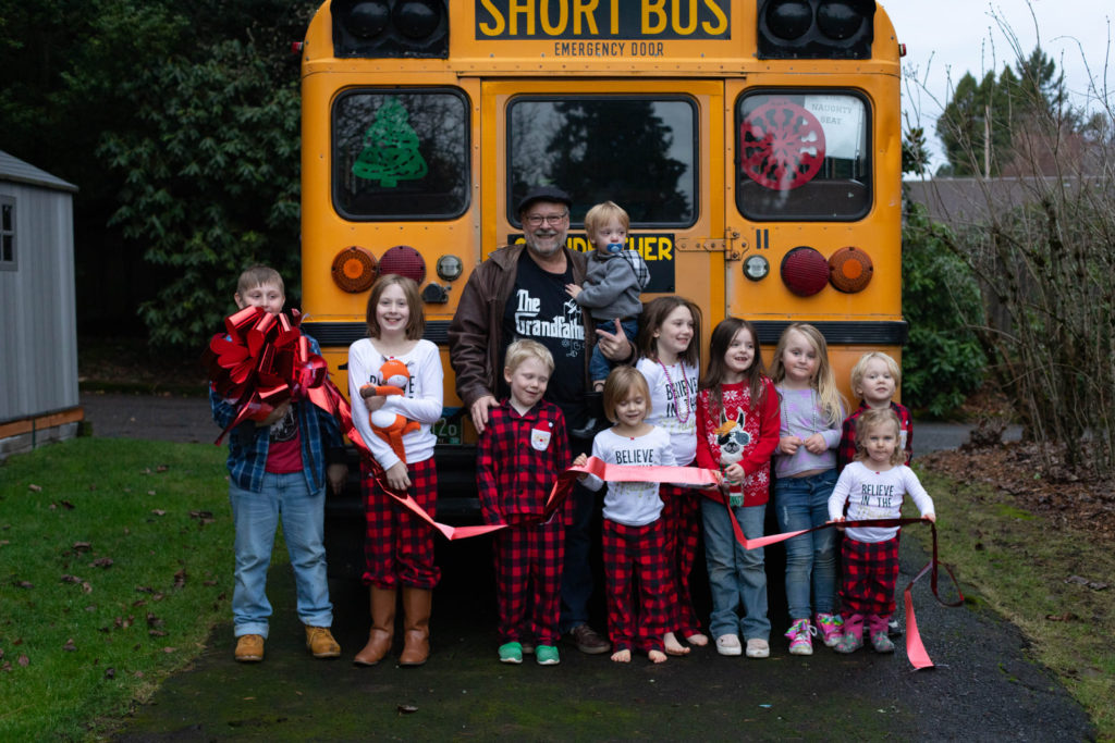Grandfather and his 10 grandkids posing in front of the school bus he purchased to drive them all to school