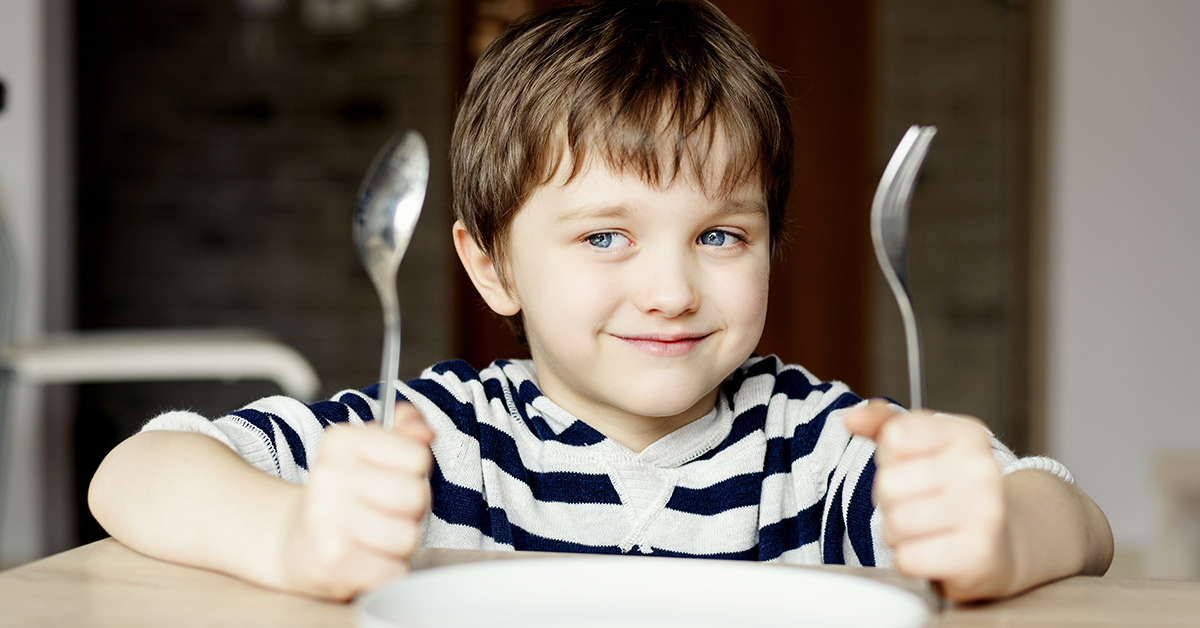 young boy holding a spoon and fork sitting at a table