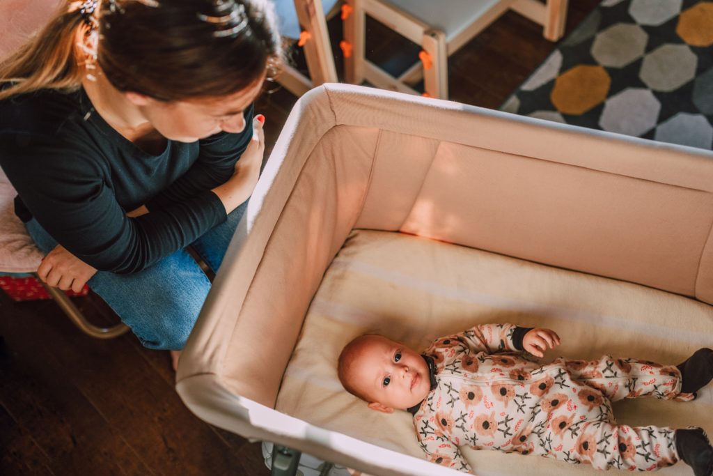 Smiling mother stands over her baby in a bassinet