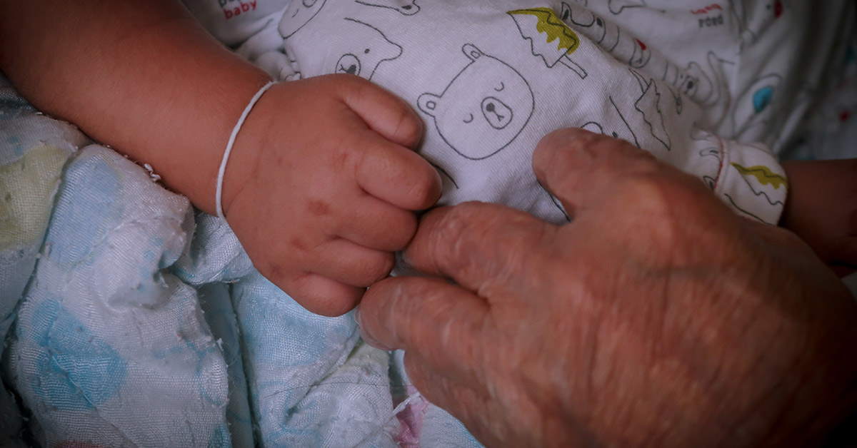 an elderly persons hand touching an infant's