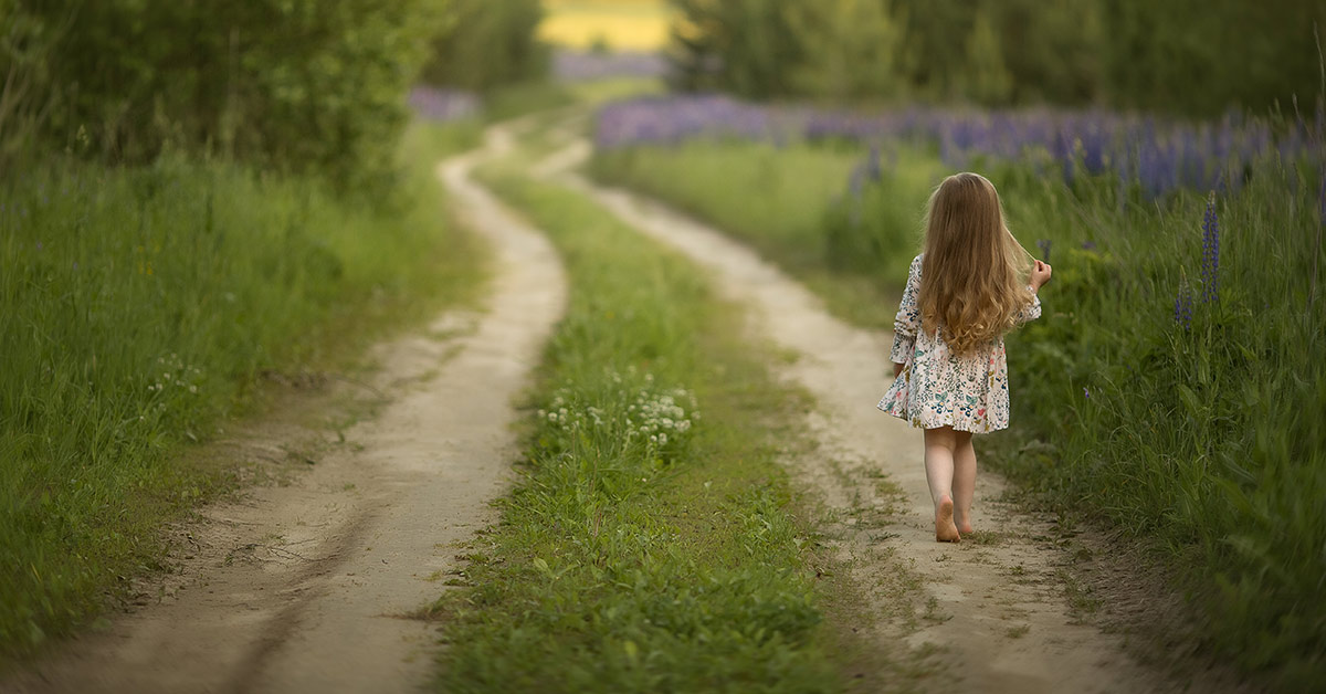 little girl walking down a grassy backroad