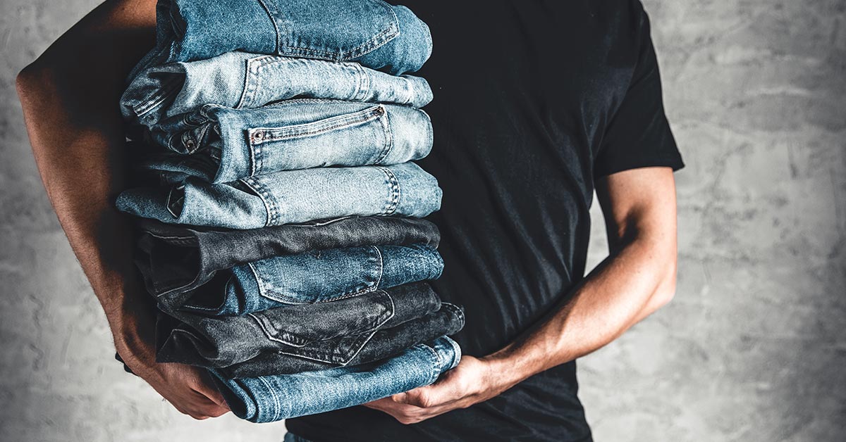 person holding a stack of several pairs of jeans