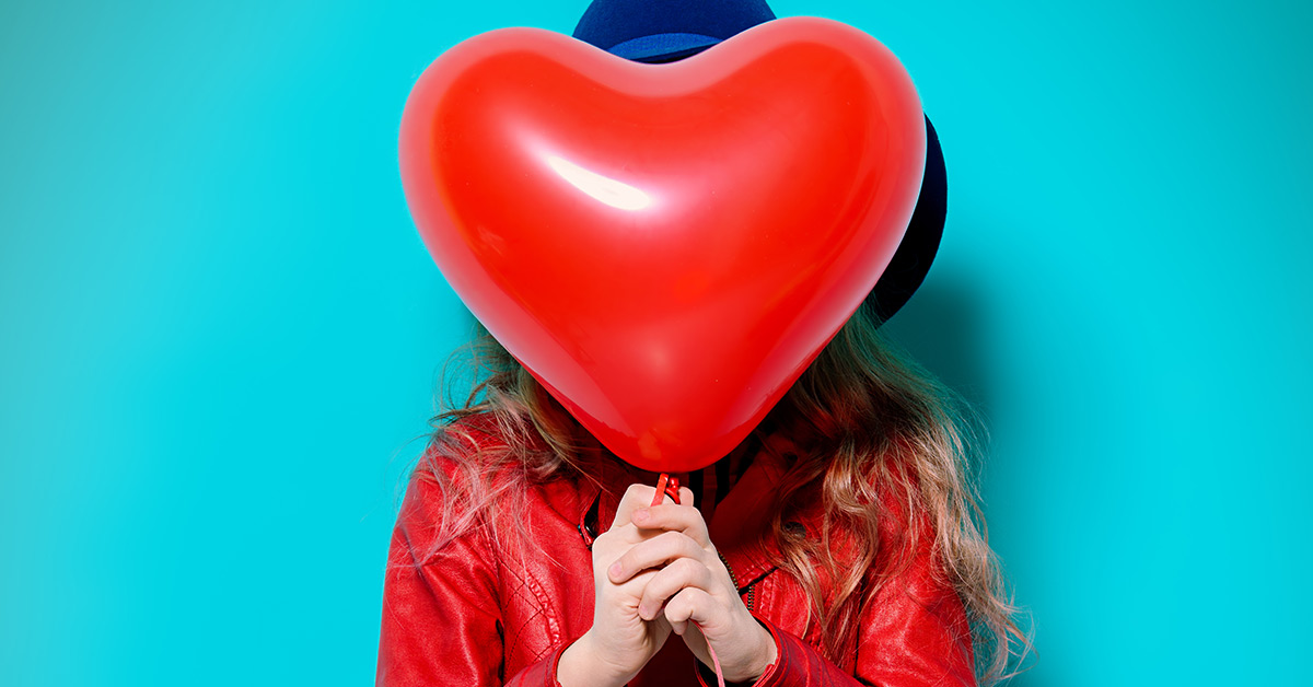 girl holding heart shaped balloon over face