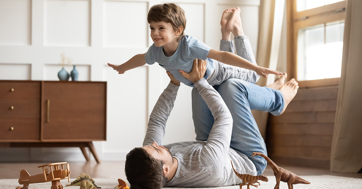 father playing with his son, laying on the floor and lifting him into the air