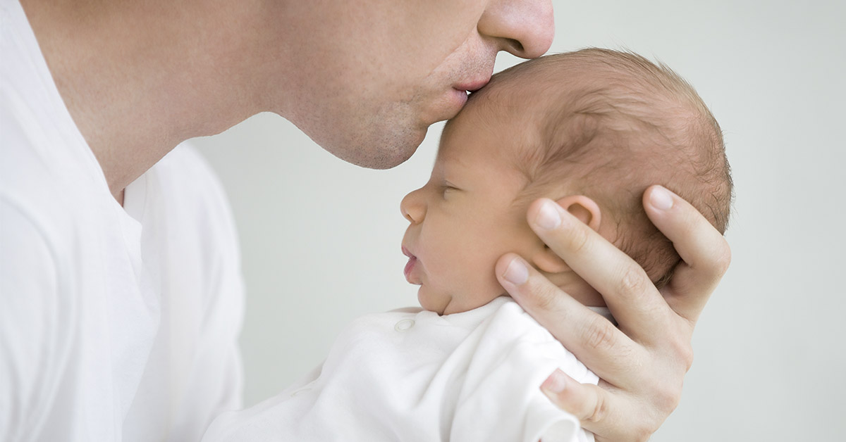 father kissing infant on forehead