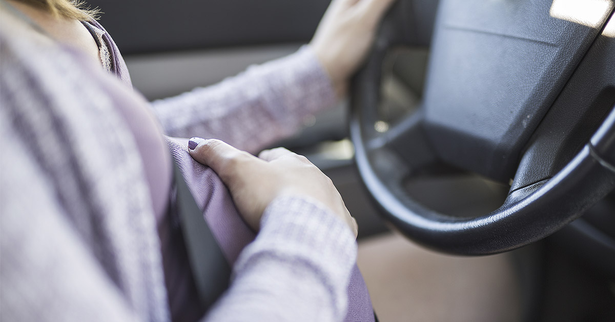 pregnant person holding belly while sitting in drivers seat and holding steering wheel