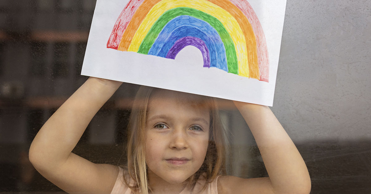 young girl holding up a drawing of a rainbow