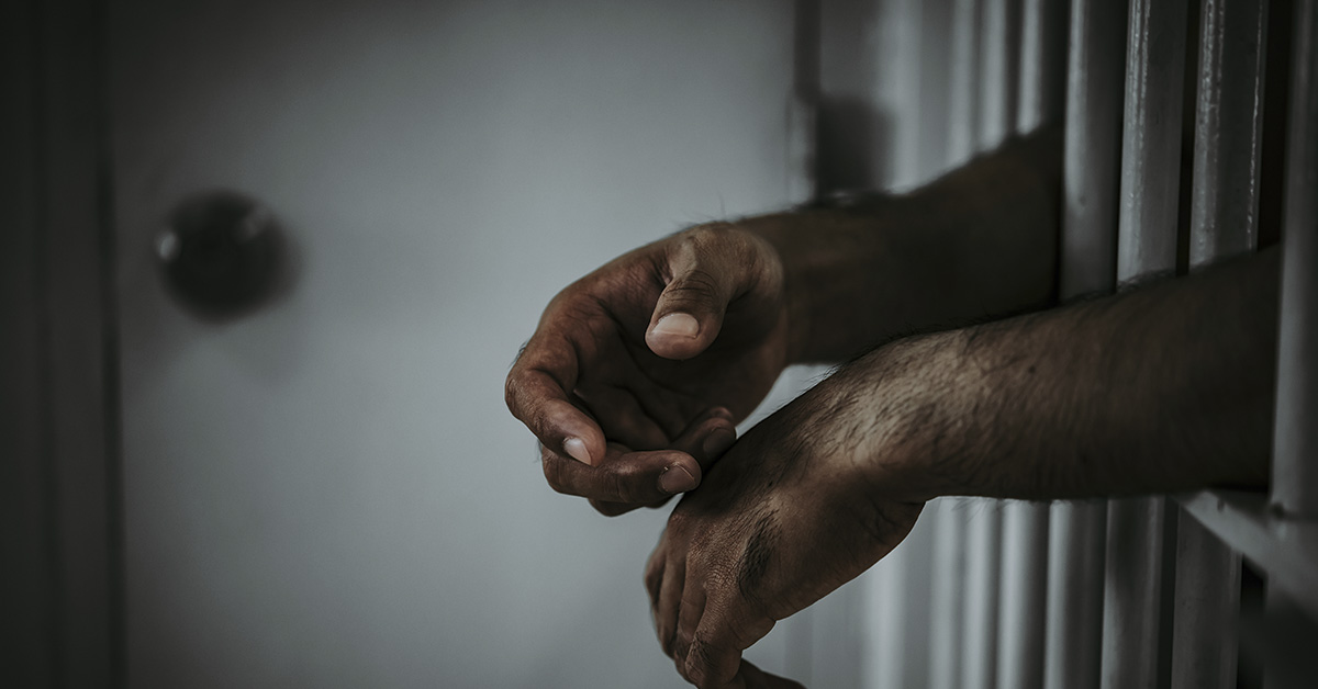 pair of male hands sticking out from a prison cell door