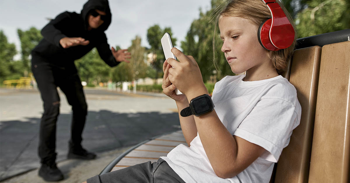 child sitting on park bench on smart phone while lurking bad man watches
