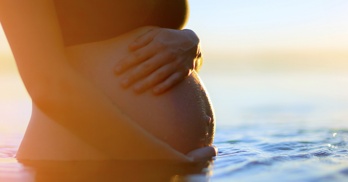 woman holding her pregnant belly while standing in a body of water