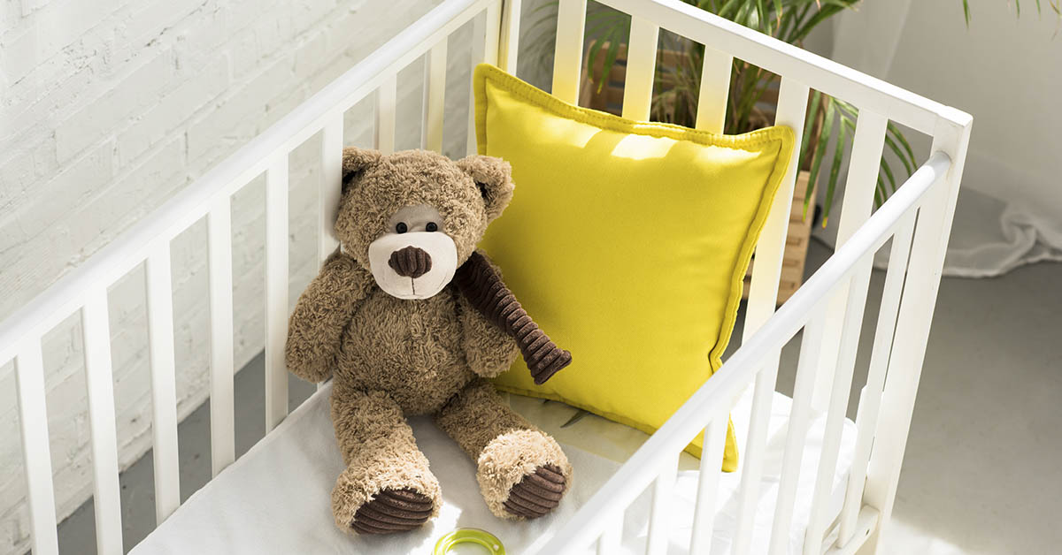 white crib containing a stuffed bear and and yellow pillow