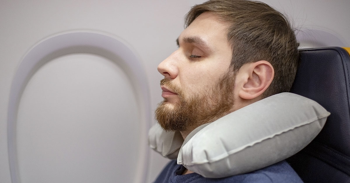man with neck pillow resting on plane