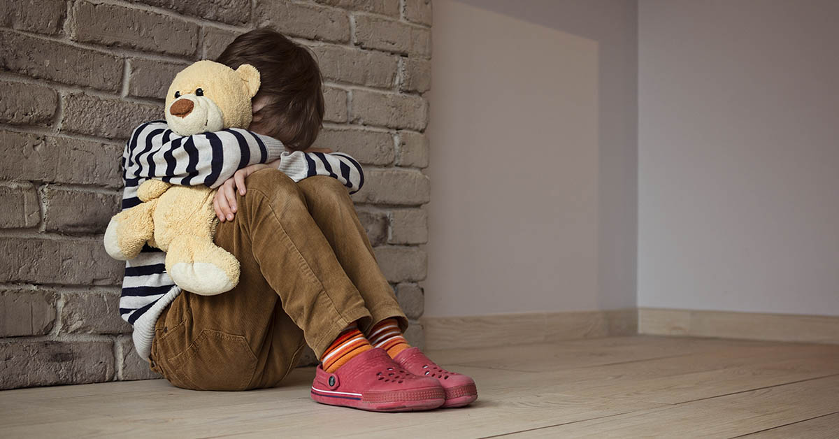 sad child sitting holding stuffed bear
