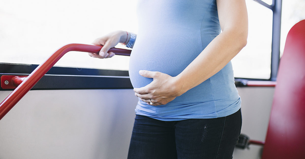 pregnant woman bracing herself while standing on a city bus