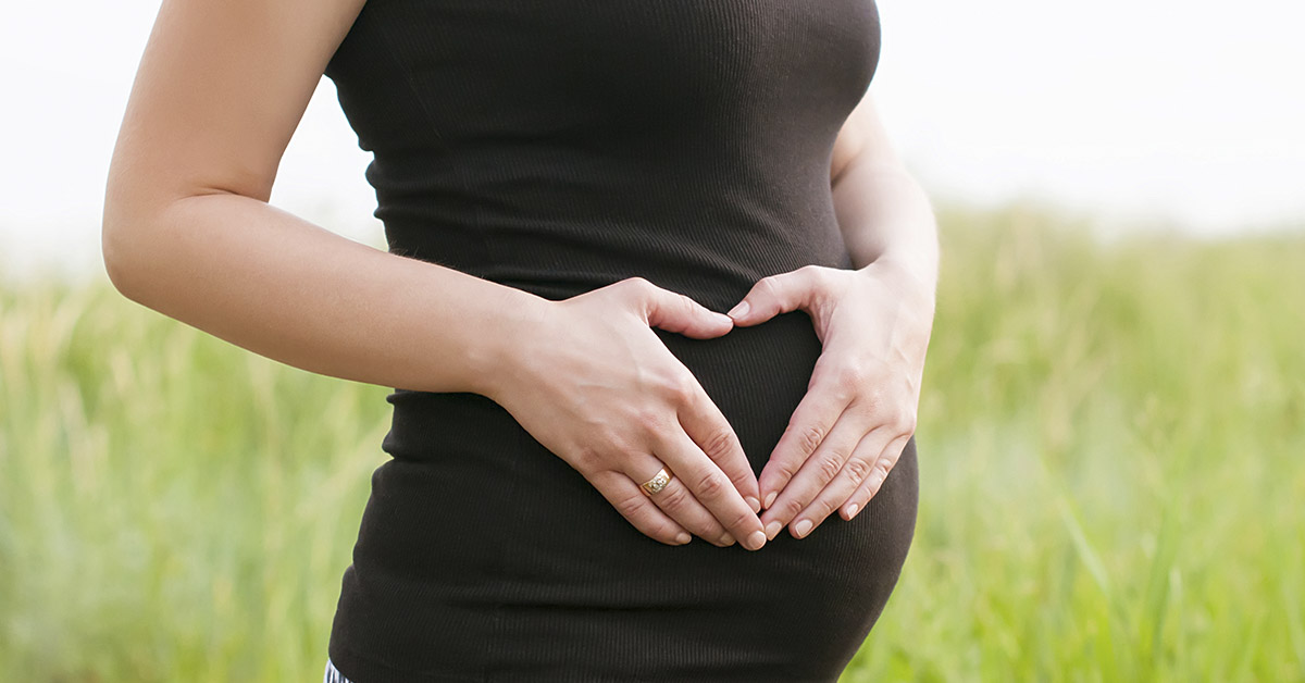 pregnant woman wearing a black dress placing hands over belly in shape of heart