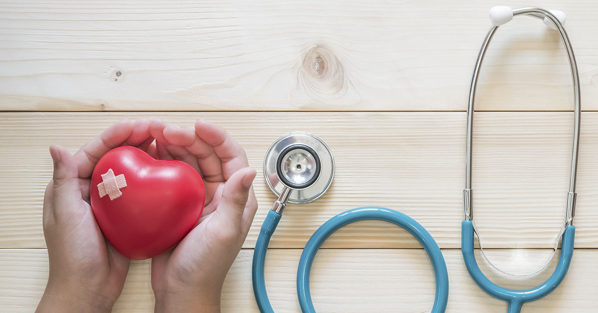 heart shape in hands with stethoscope on wooden table