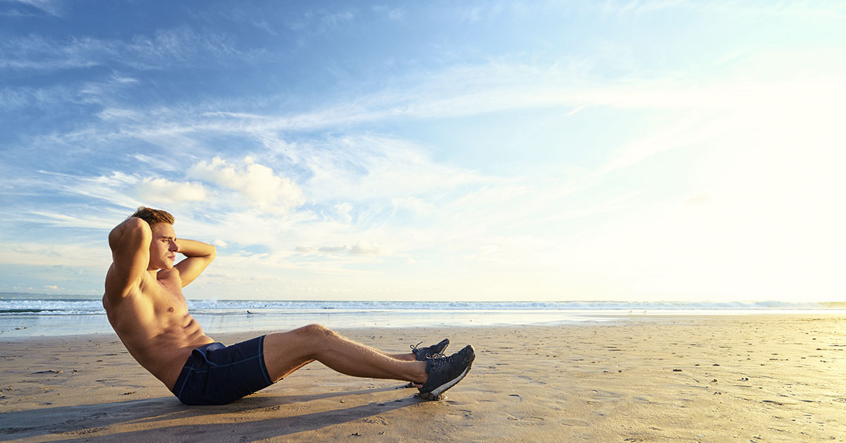 man doing sit ups shirtless on beach
