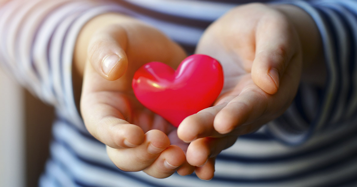 a child's hand holding a red heart
