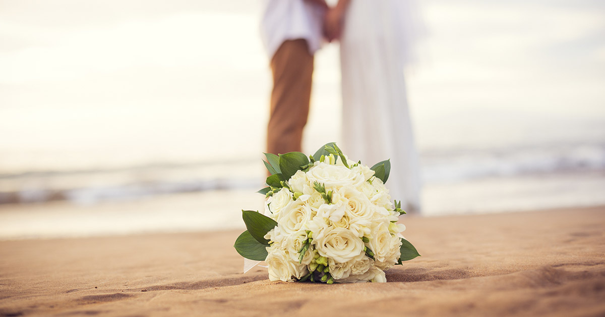 bouquet of white flowers laying on a beach, a couple is being wed in the background