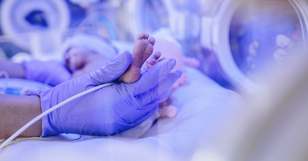 hand with medical gloves holding infants small foot in hospital setting