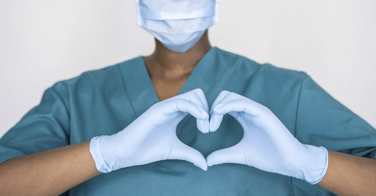 nurse in scrubs and latex gloves forming the shape of a heart with their hands