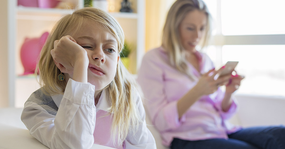 Parent phubbing her child using smartphone in background ignoring child in foreground