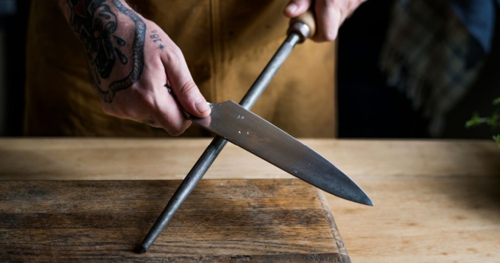 person sharpening a chef's knife over wooden cutting board 