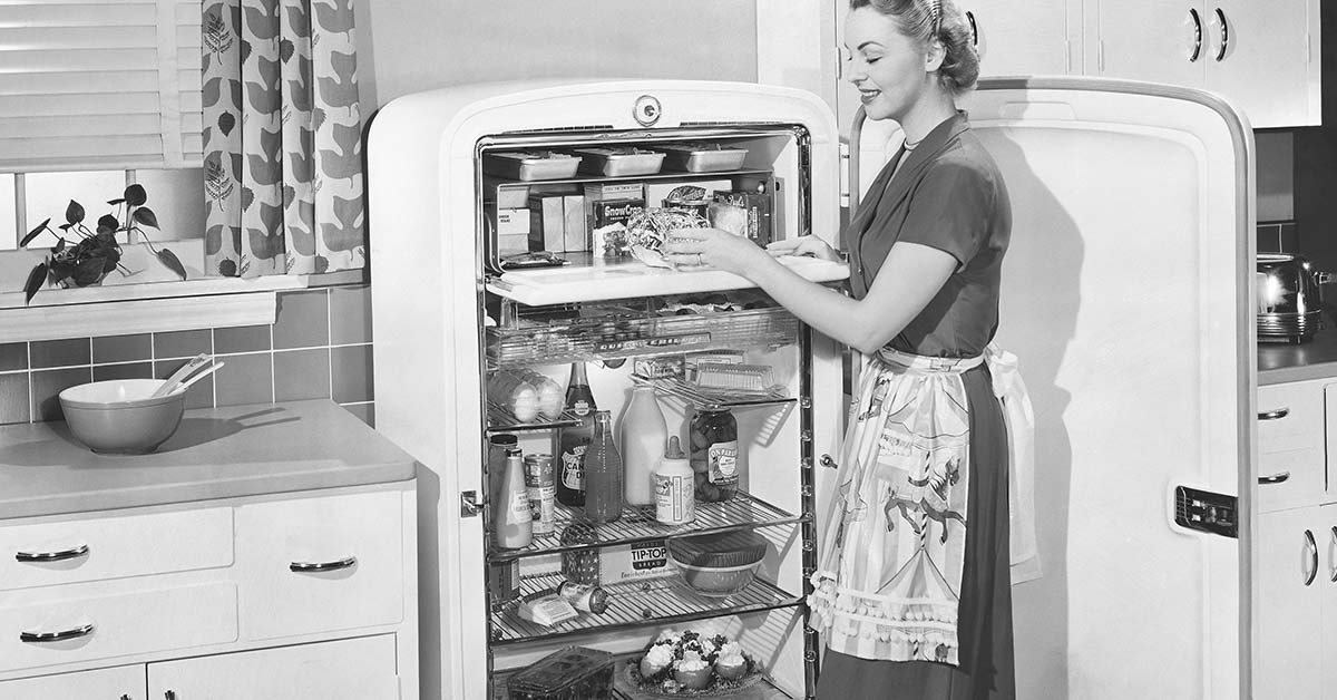 vintage black and white image of woman looking through a refrigerator in a home kitchen