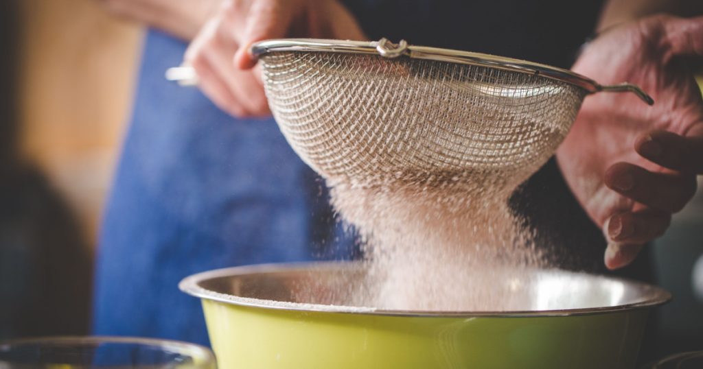 Close up image of a chef sifting together flour and ingredients to bake a delicious cake.