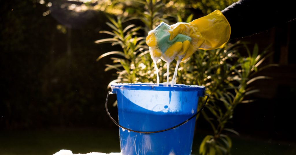Spring Cleaning outside with big yellow cleaning gloves, water, soap and a big blue bucket with soap