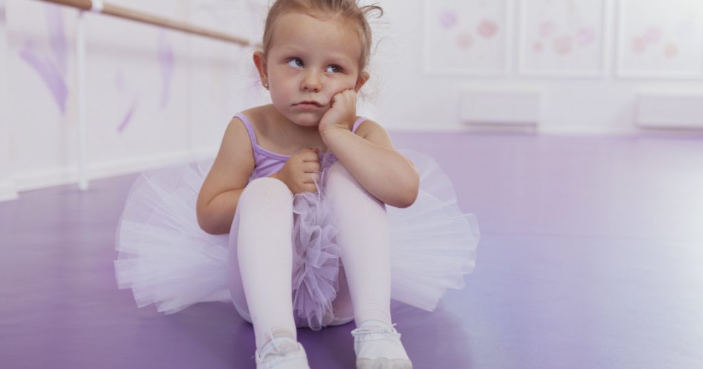 Cute little funny ballerina girl looking away with annoyed expression, copy space. Adorable little ballerina looking tired and bored at ballet class. Unhappy, angry child concept