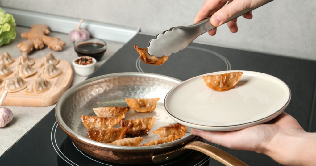 Woman serving freshly cooked delicious gyoza on plate in kitchen, closeup
