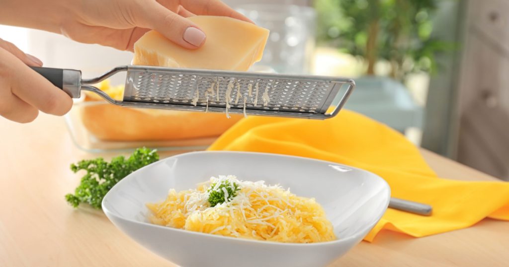 Woman grating cheese on spaghetti squash in plate
