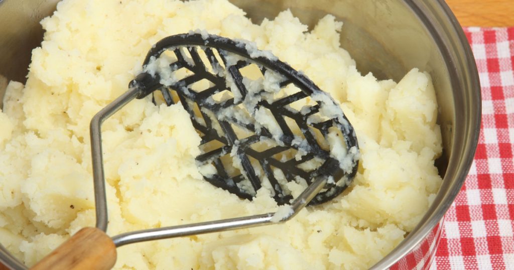 Freshly mashed potatoes with masher in saucepan.
