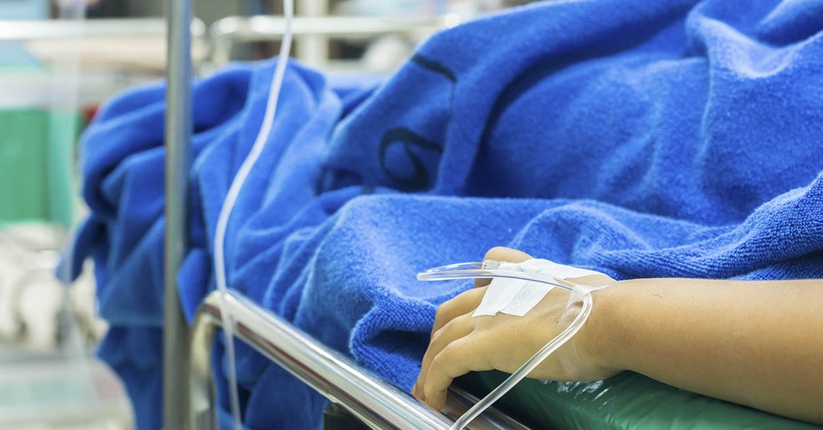 person in hospital bed with IV inserted in hand