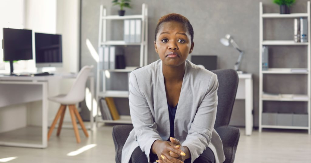 Portrait of black business woman in suit sitting on office chair looking at you with face expression that could be interpreted as both disappointed unimpressed and impressed 'Hmm not bad' expression
