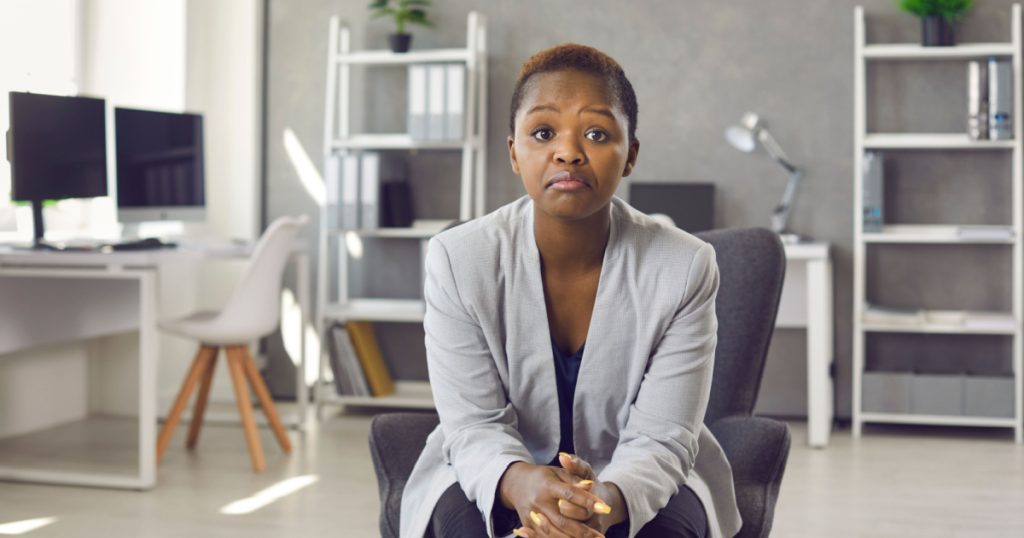 Portrait of black business woman in suit sitting on office chair looking at you with face expression that could be interpreted as both disappointed unimpressed and impressed 'Hmm not bad' expression