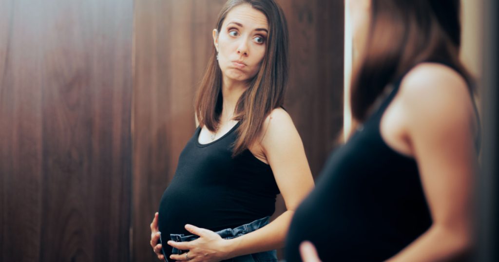 Pregnant Woman Unable to Close Pants in need for Maternity Clothes. Stressed mother to be seeing her body image change in pregnancy