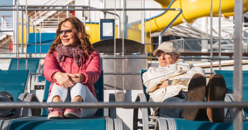 beautiful happy middle aged couple relaxing on deck chairs of a cruise ship - travel and vacation concept
