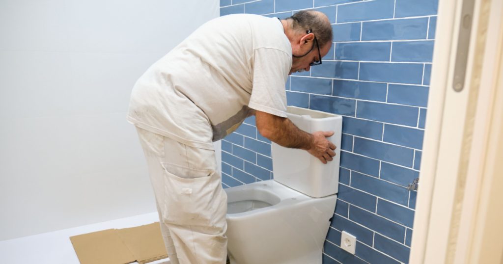 Senior plumber installer installing toilet cistern in a bathroom.
